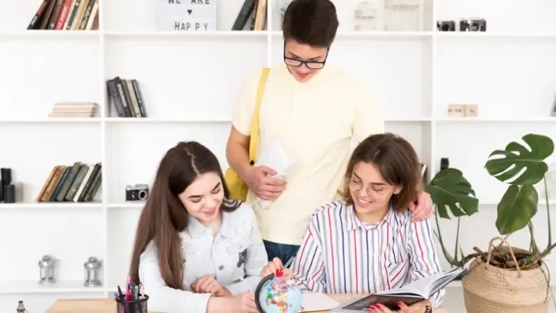 A group of three people engaged in studying, surrounded by books, a globe, and a potted plant in a bright, modern room A group of three people engaged in studying, surrounded by books, a globe, and a potted plant in a bright, modern room
